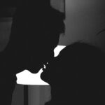 Silhouette of a couple kissing in a romantic and intimate moment against a bright light.