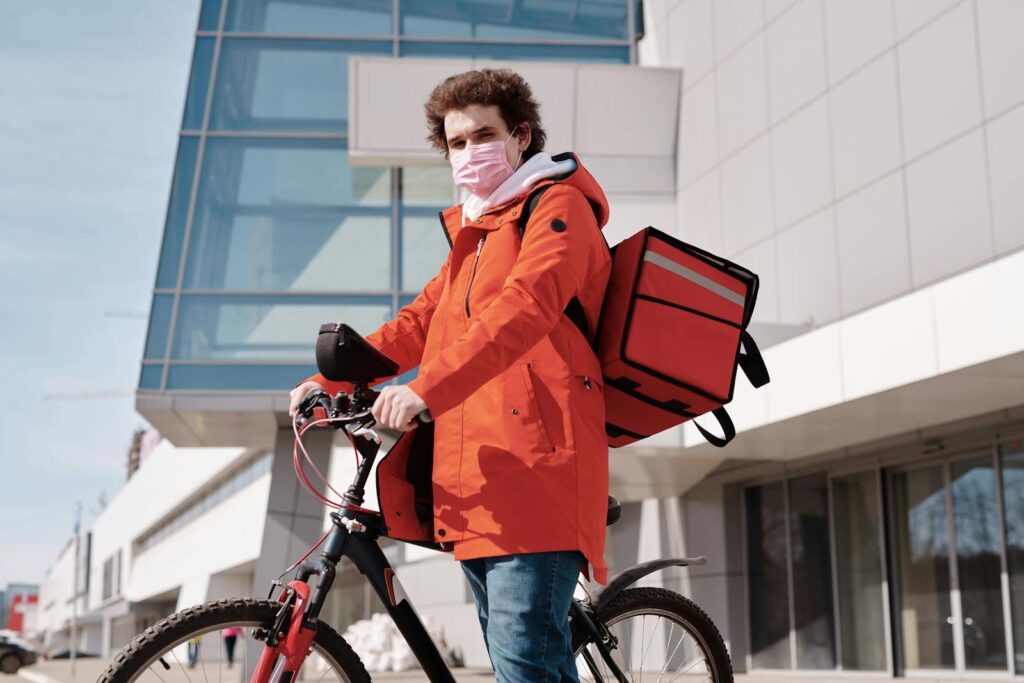 An urban cyclist wearing a face mask and carrying a thermal bag for food delivery, outdoors.