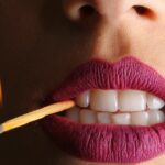 Bold close-up of lips with vivid lipstick holding a lit matchstick, creating a fierce and dynamic image.